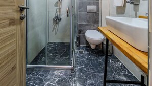 A modern bathroom with a glass-enclosed shower, a toilet, and a sink with a wooden countertop. - La Pazza Suites (Istanbul)