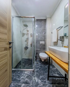 A modern bathroom with a glass-enclosed shower, a toilet, and a sink with a wooden countertop. - La Pazza Suites (Istanbul)