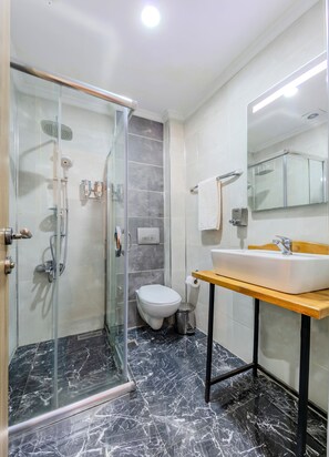 Une salle de bain moderne avec une douche à parois de verre, des toilettes, un lavabo doté d'un plan de travail en bois et un miroir.