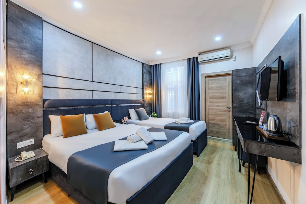 A modern hotel room with two beds, a desk, a TV, and an air conditioning unit.