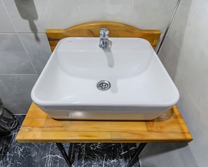 Un baño con un lavamanos blanco sobre un mueble de madera, un cabecero de madera y paredes con azulejos.