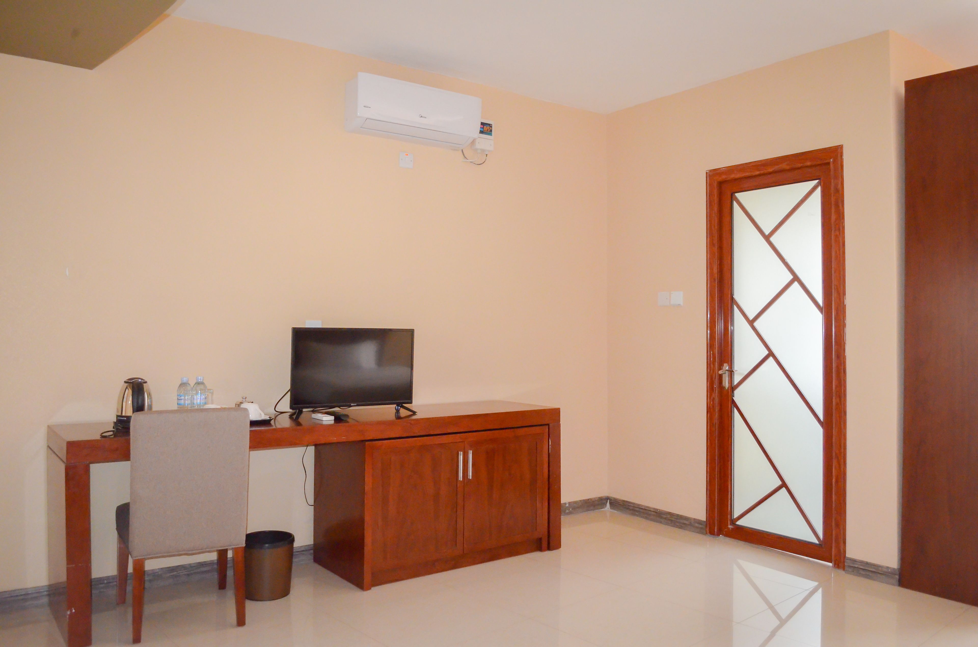 A room with a wooden desk, a television, a chair, a trash bin, and a door with a geometric glass design.