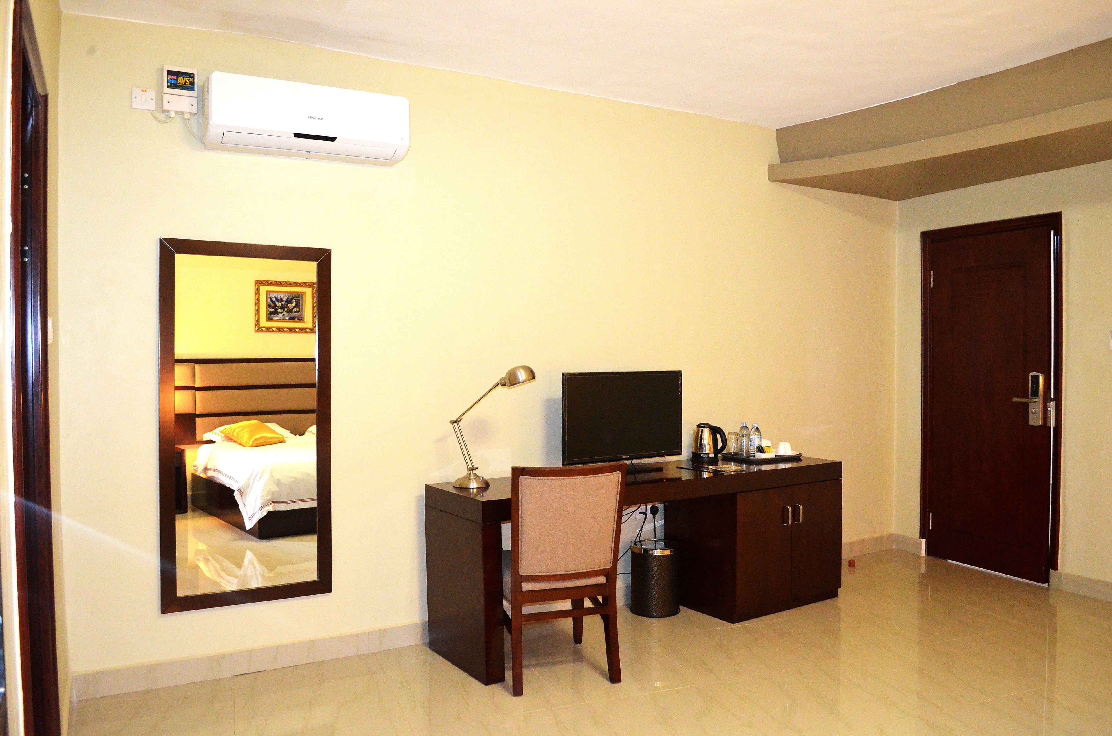 Quarto de hotel com cama, secretária com computador, cadeira, televisão e porta.