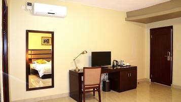 Quarto de hotel com cama, secretária com computador, cadeira, televisão e porta.