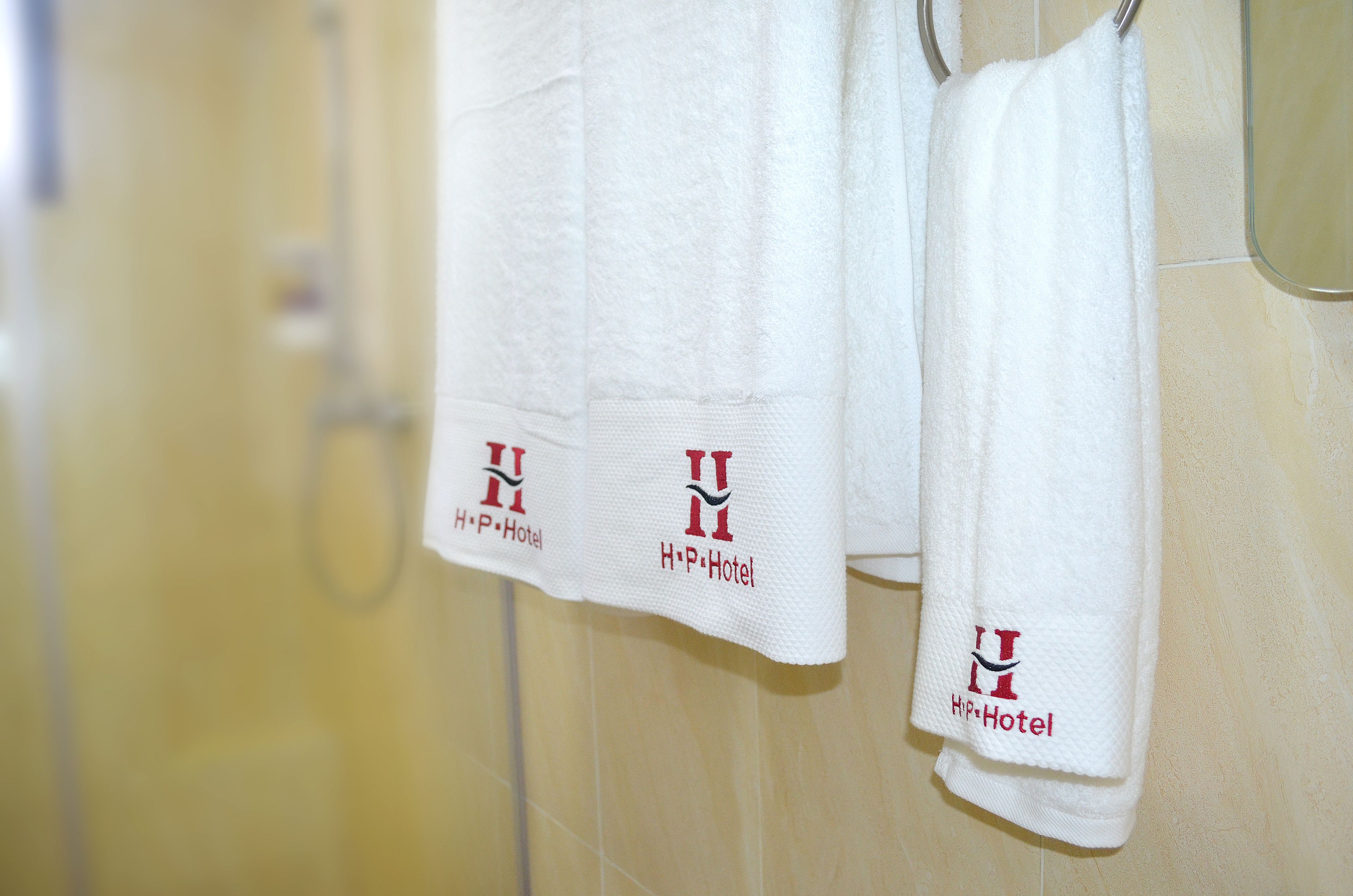 Two white towels with "H.P. Hotel" logo hanging on a tiled wall.