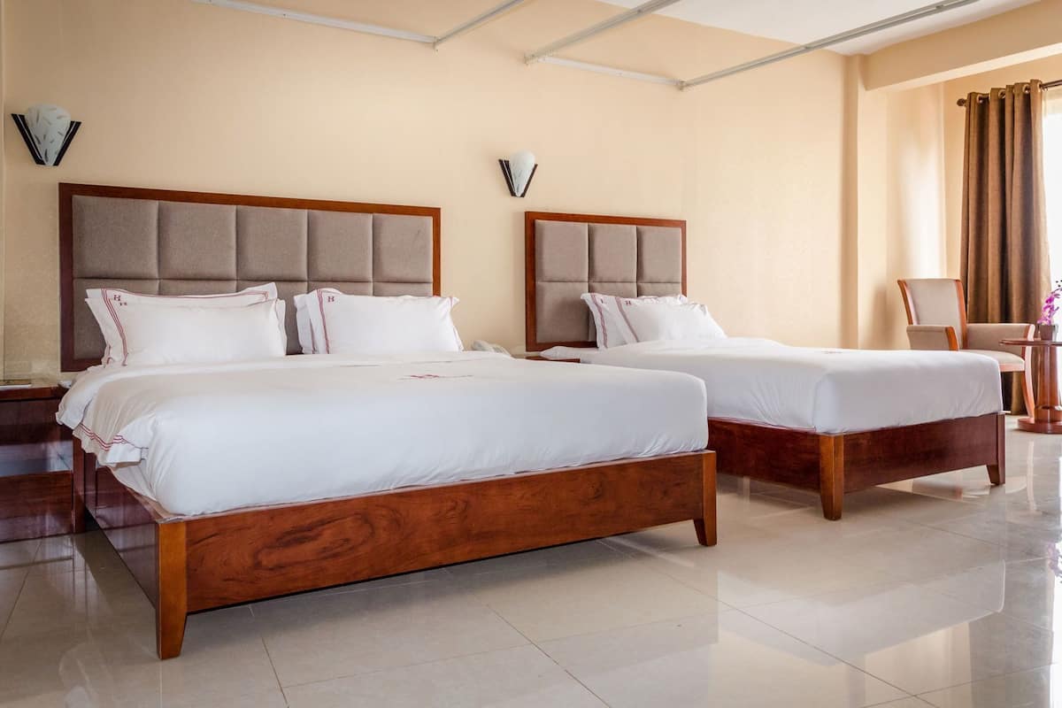 A hotel room with two beds, a wooden headboard, a nightstand, a chair, and a small table with a vase of flowers.