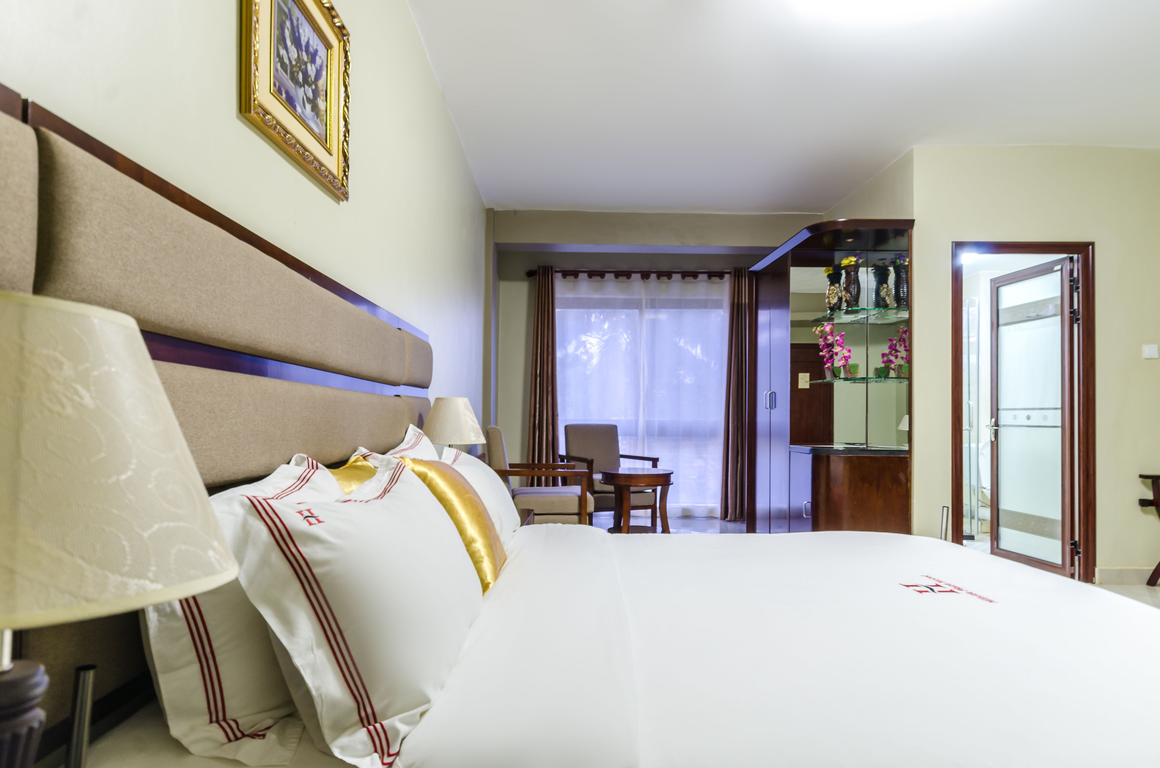 A hotel room with a large bed, a desk, a chair, and a view of the outdoors.