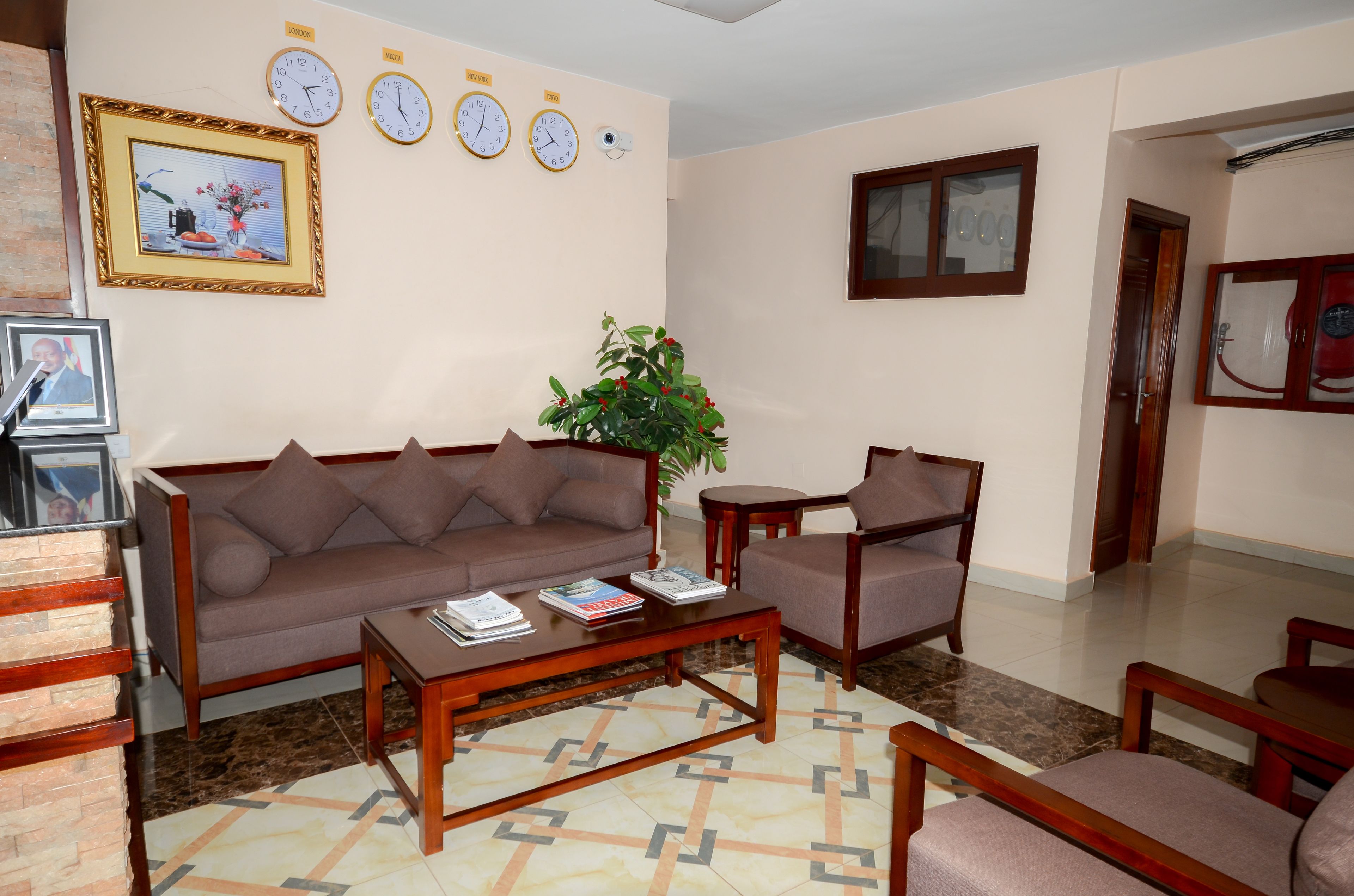A living room with a brown sofa, a wooden coffee table, and a chair. There are clocks on the wall and a framed picture.