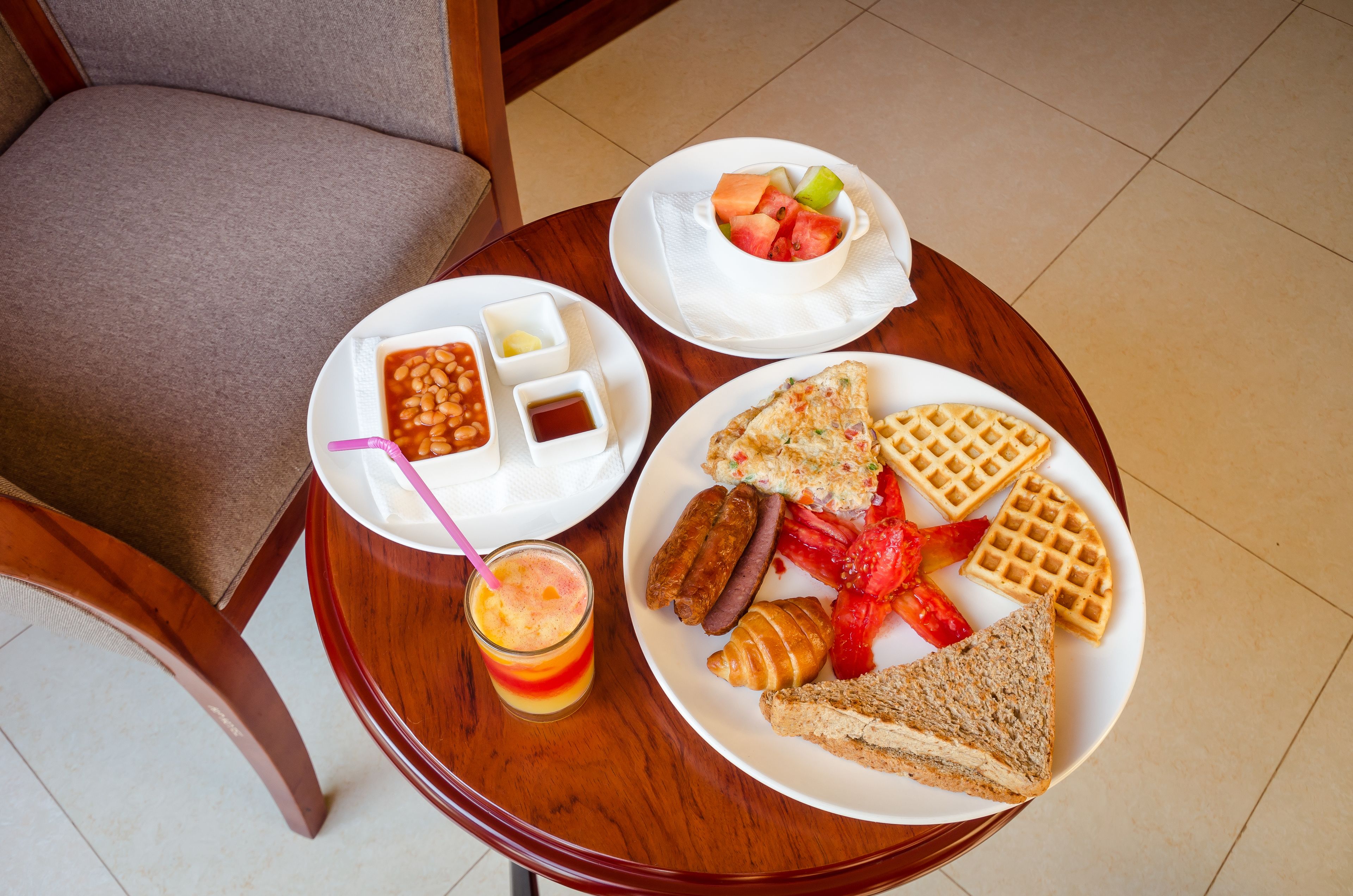 A breakfast table with plates of food including beans, toast, waffles, and a fruit bowl.