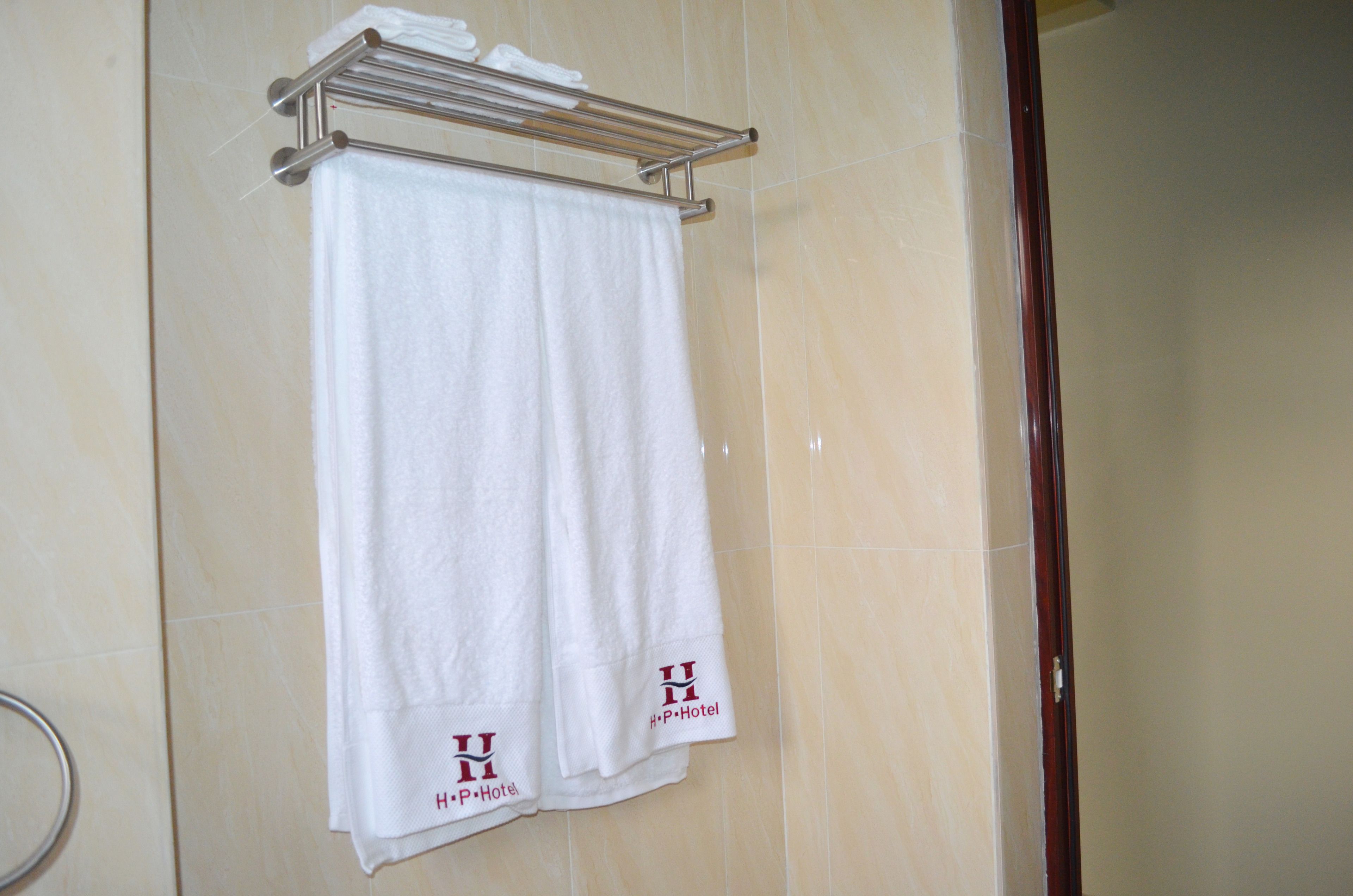 A white towel hanging on a metal rack in a bathroom with beige tiles.
