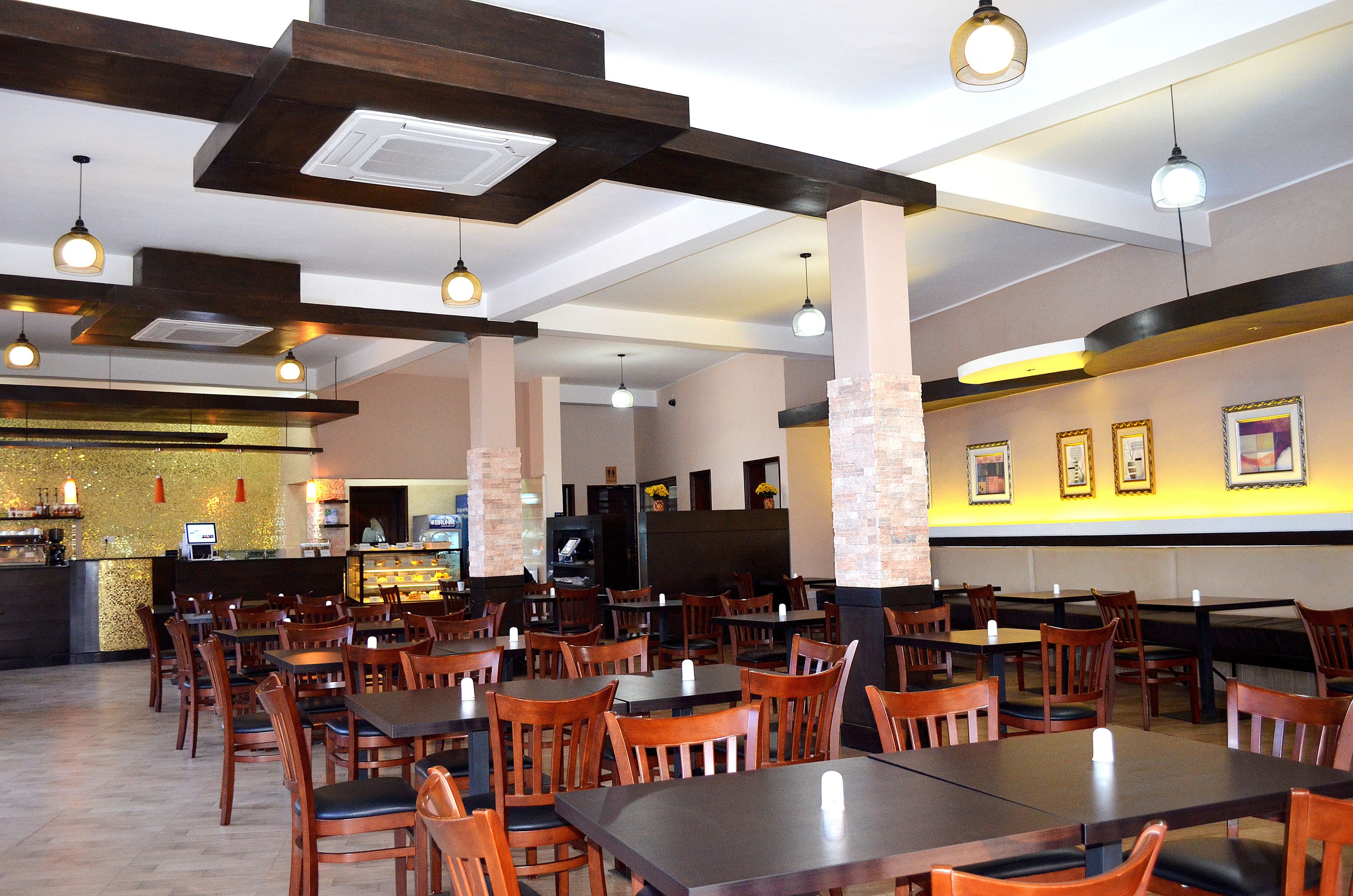 A restaurant with wooden tables and chairs, a bar area, and a wall with framed pictures.