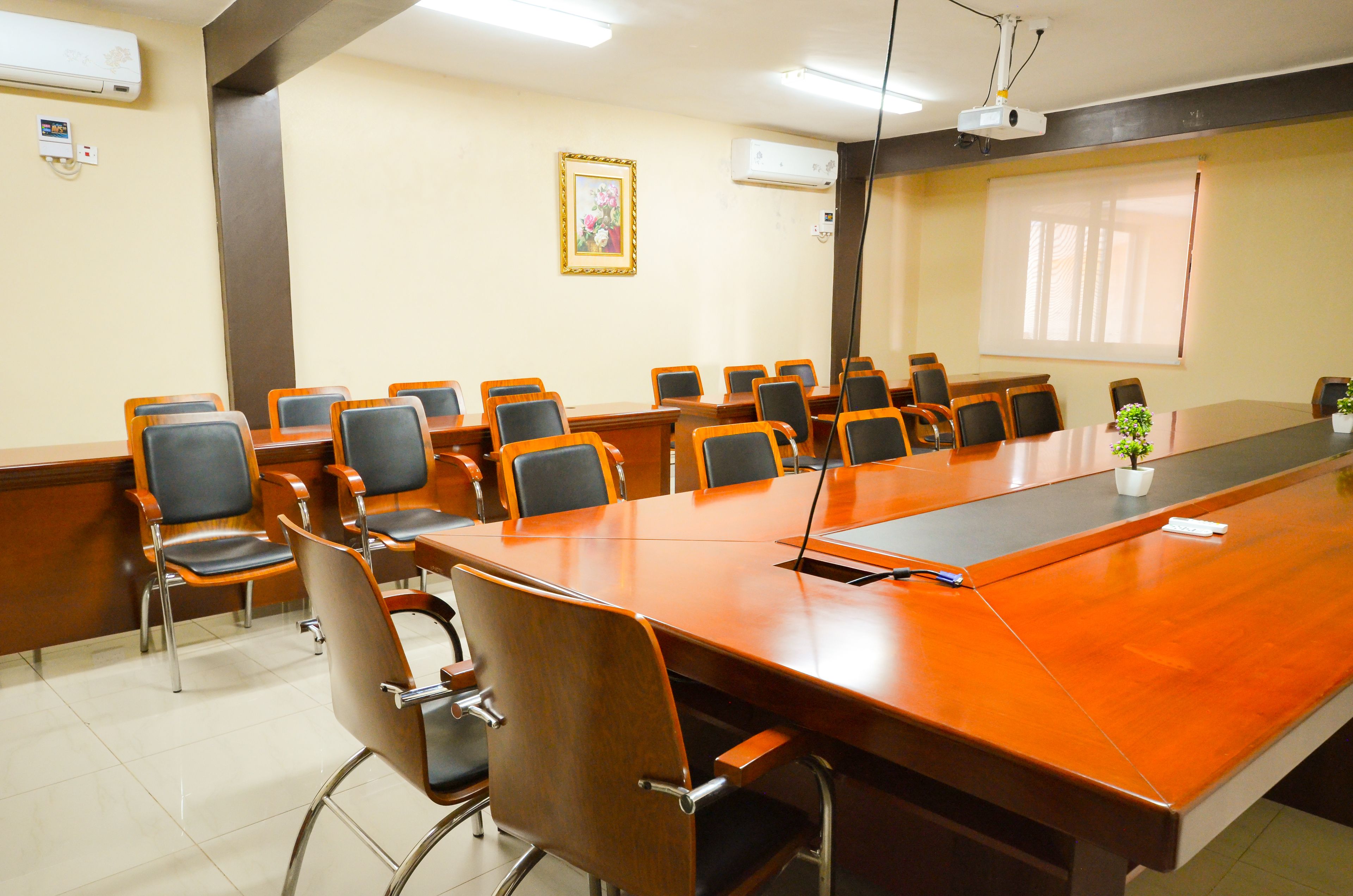 A conference room with a long wooden table, multiple chairs, a projector, and a framed picture on the wall.