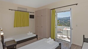 Een slaapkamer met twee bedden, een garderobe, een balkon met een tafel en stoel, en uitzicht op het landschap.