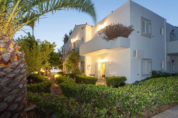 A modern two-story building with a white exterior, surrounded by well-maintained greenery and a palm tree.