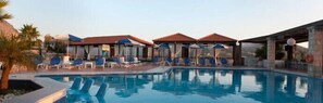 A swimming pool with lounge chairs and umbrellas, surrounded by covered areas.