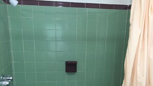 A bathroom with green tiled walls, a dark square object on the wall, and a beige shower curtain. - Shelton Motel (Rio Grande)