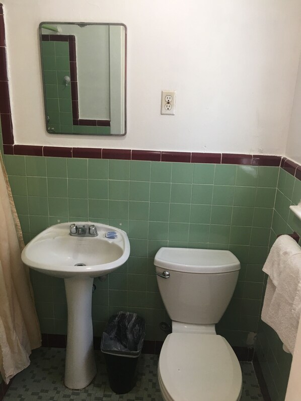 Un baño con lavamanos pedestal, inodoro, espejo y cubo de basura.