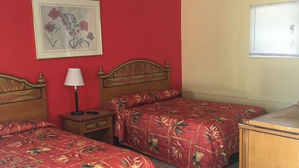 A room with two beds, a nightstand with a lamp, a wooden dresser, a ceiling fan, and a window with blinds. - Shelton Motel (Rio Grande)
