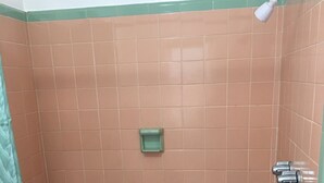 A small, enclosed shower area with a green and beige tiled wall, a small green shelf, and a showerhead. - Shelton Motel (Rio Grande)