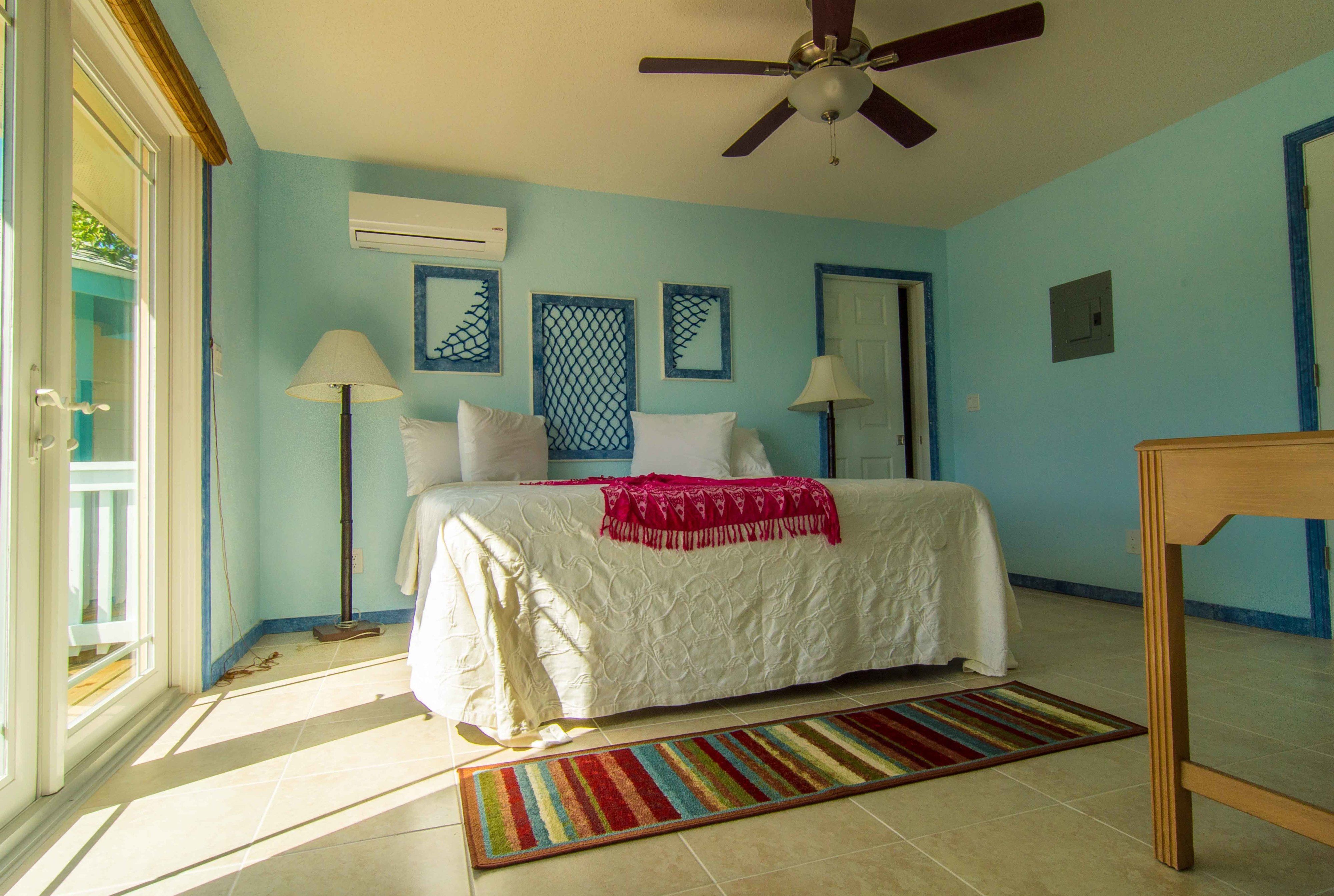 A bedroom with a bed, two bedside lamps, a ceiling fan, and a window with a view.
