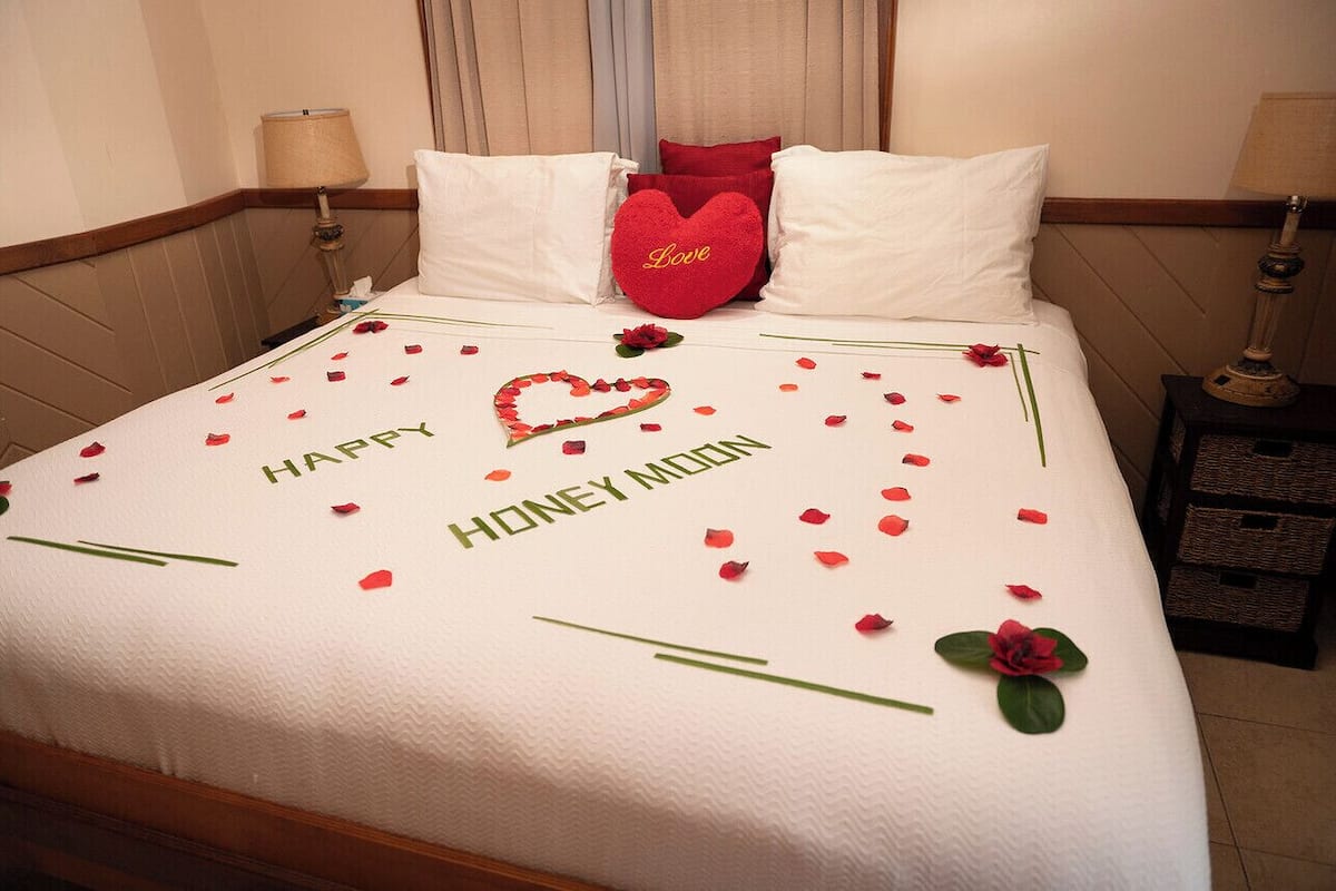 A hotel room with a bed adorned with rose petals and a 'Happy Honeymoon' message.