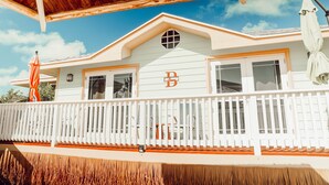 A white house with a balcony, a wooden roof, and a 'B' logo on the front. - EMBRACE Resort (Staniel Cay)