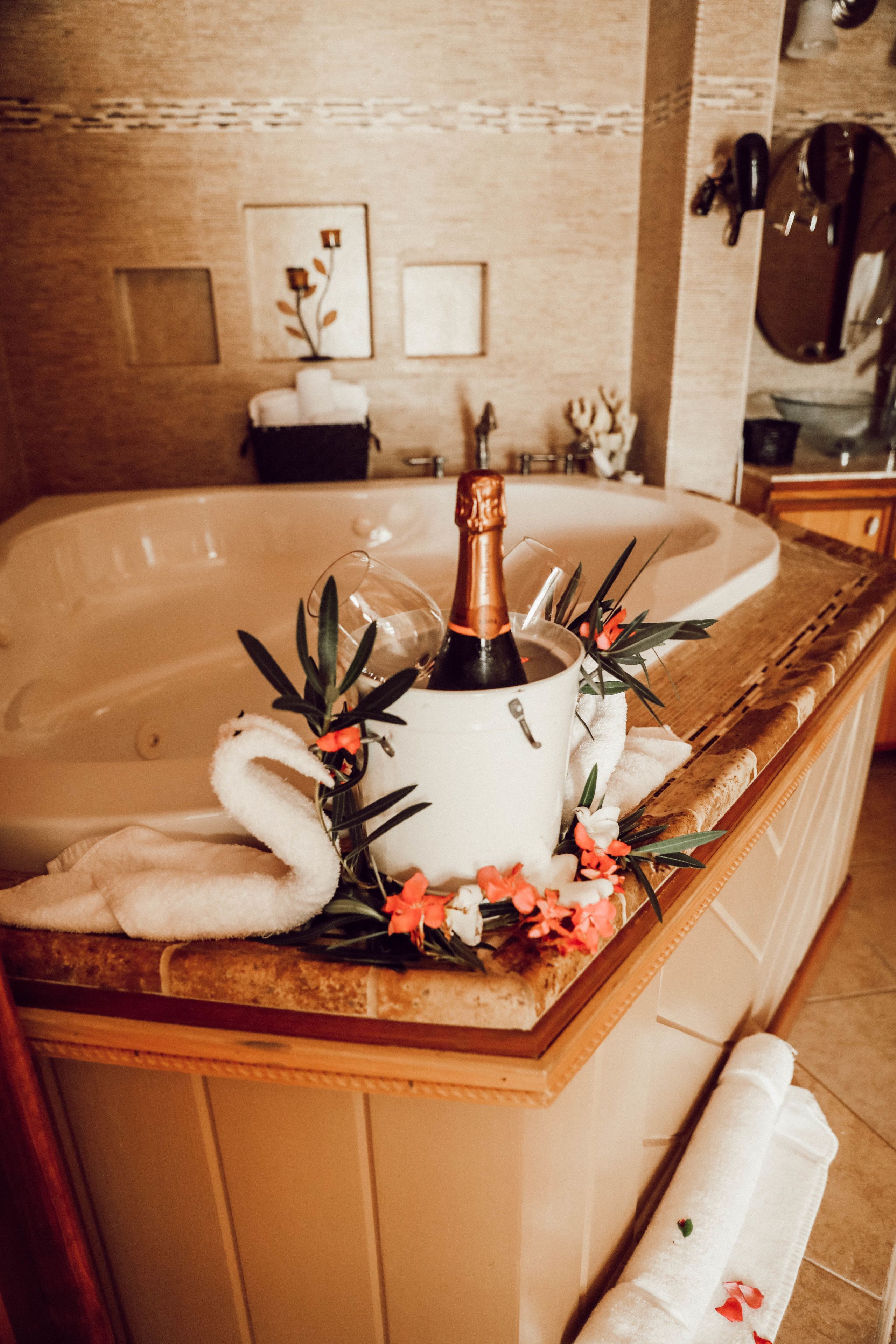 A bathroom with a large bathtub, a bottle of champagne, and decorative flowers.