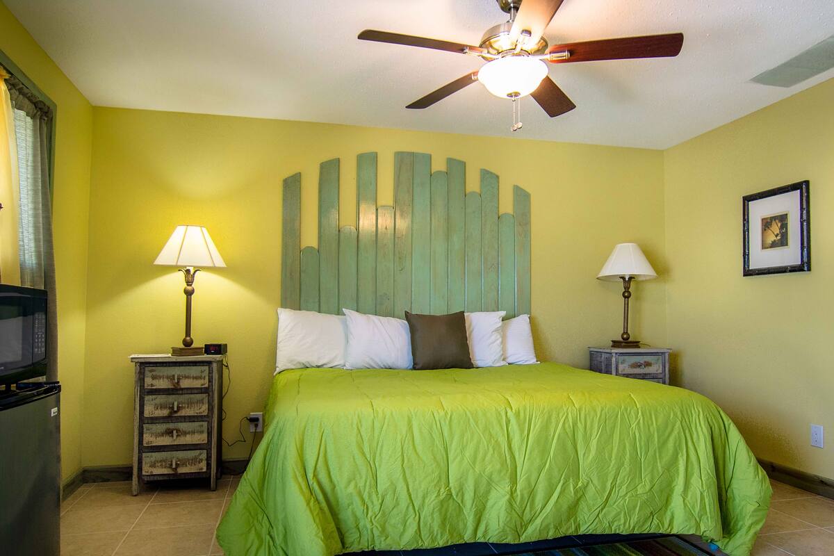 A bedroom with a bed, two bedside tables, a ceiling fan, and a wall-mounted picture.