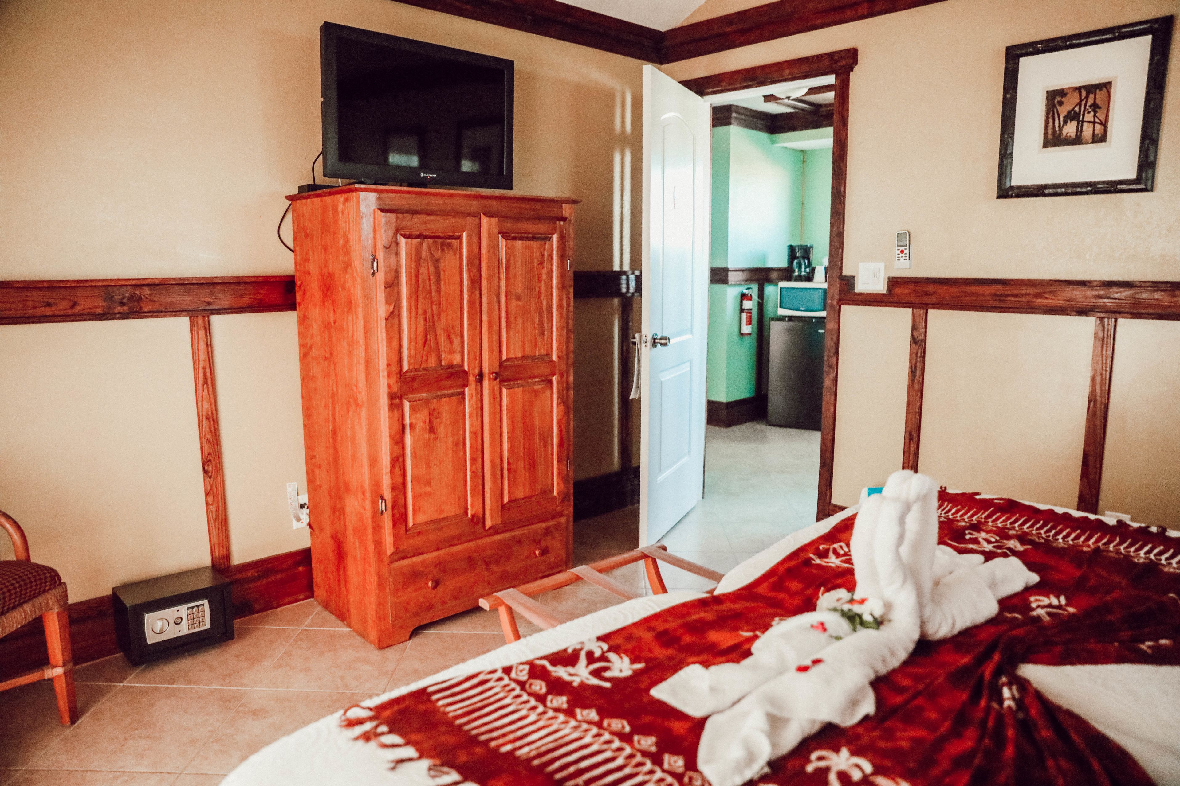 Een hotelkamer met een houten garderobe, een bed met een rood-witte spreideken en een televisie bovenop de garderobe.
