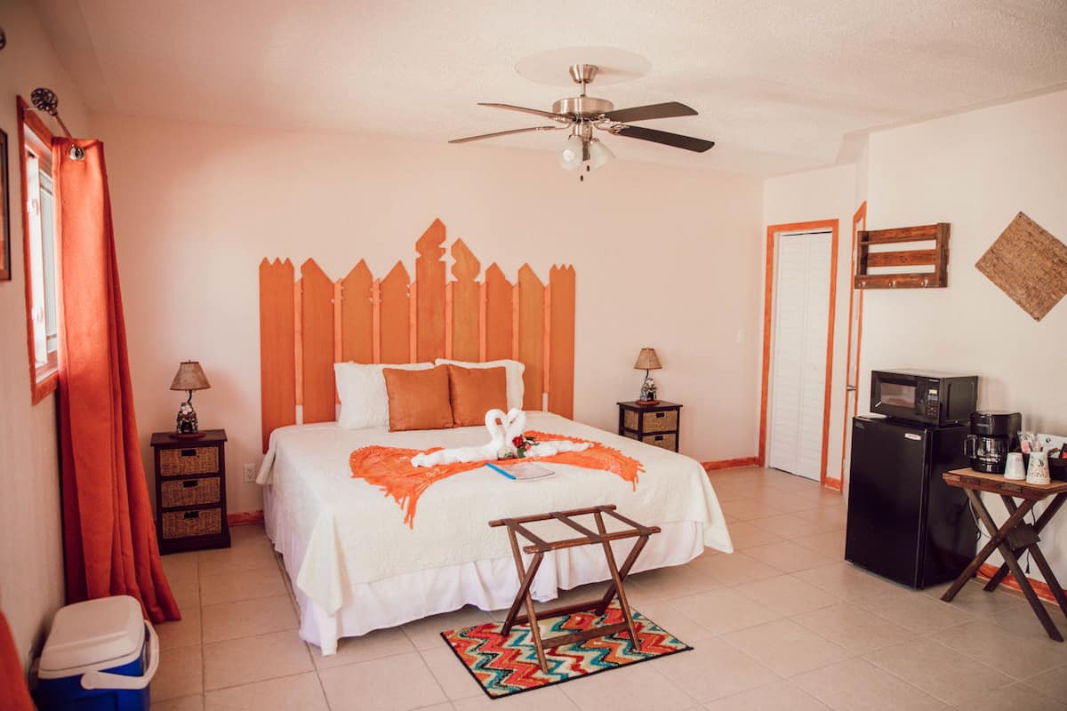 A hotel room with a bed, a ceiling fan, a microwave, a refrigerator, and a small table with a coffee maker.