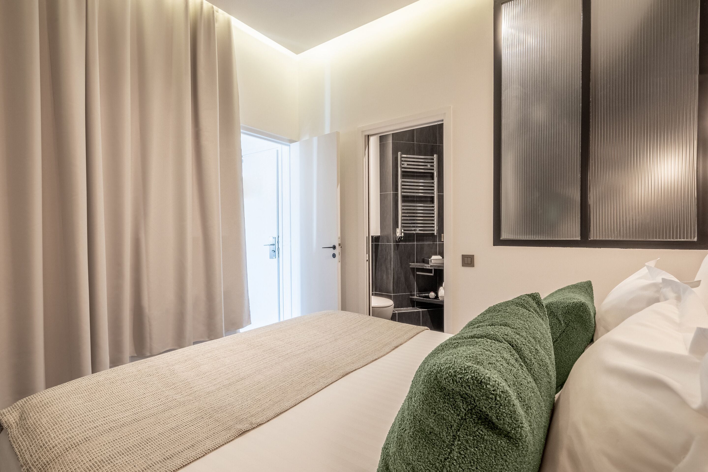 A modern hotel room with a large bed, a green throw blanket, and a walk-in closet with a mirror.