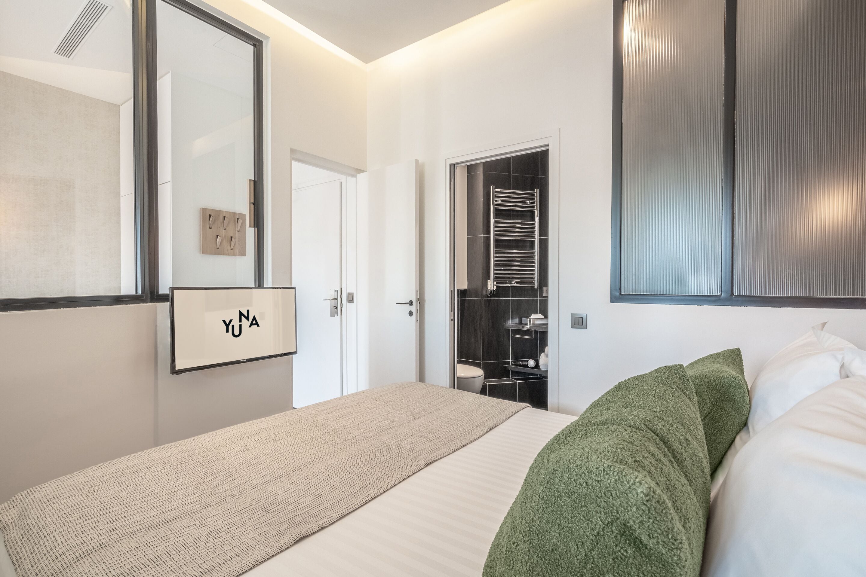 A modern bedroom with a large bed, a wardrobe, and a bathroom visible through an open door.