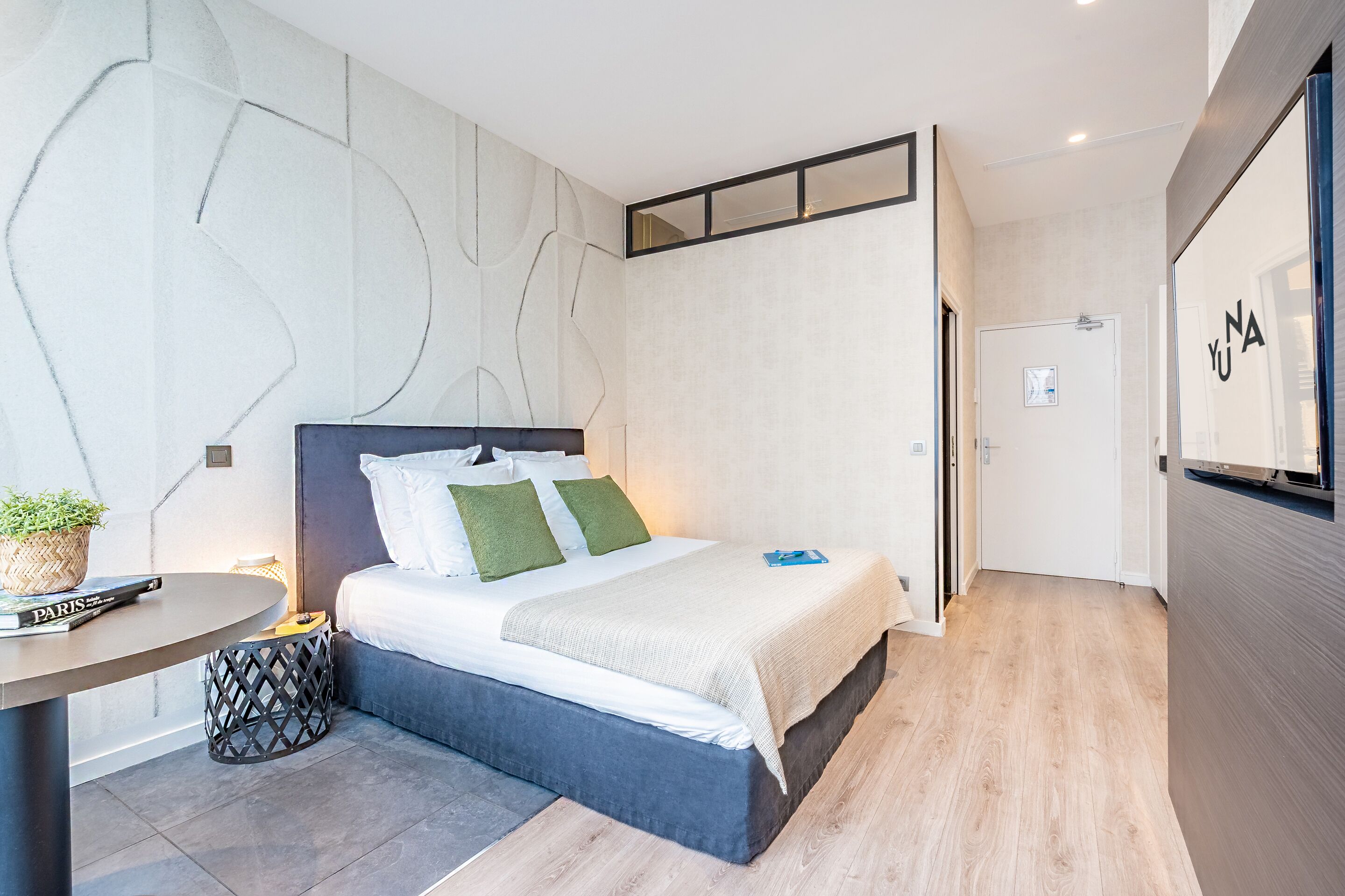A modern bedroom with a bed, bedside table, and a small round table with a plant and book.