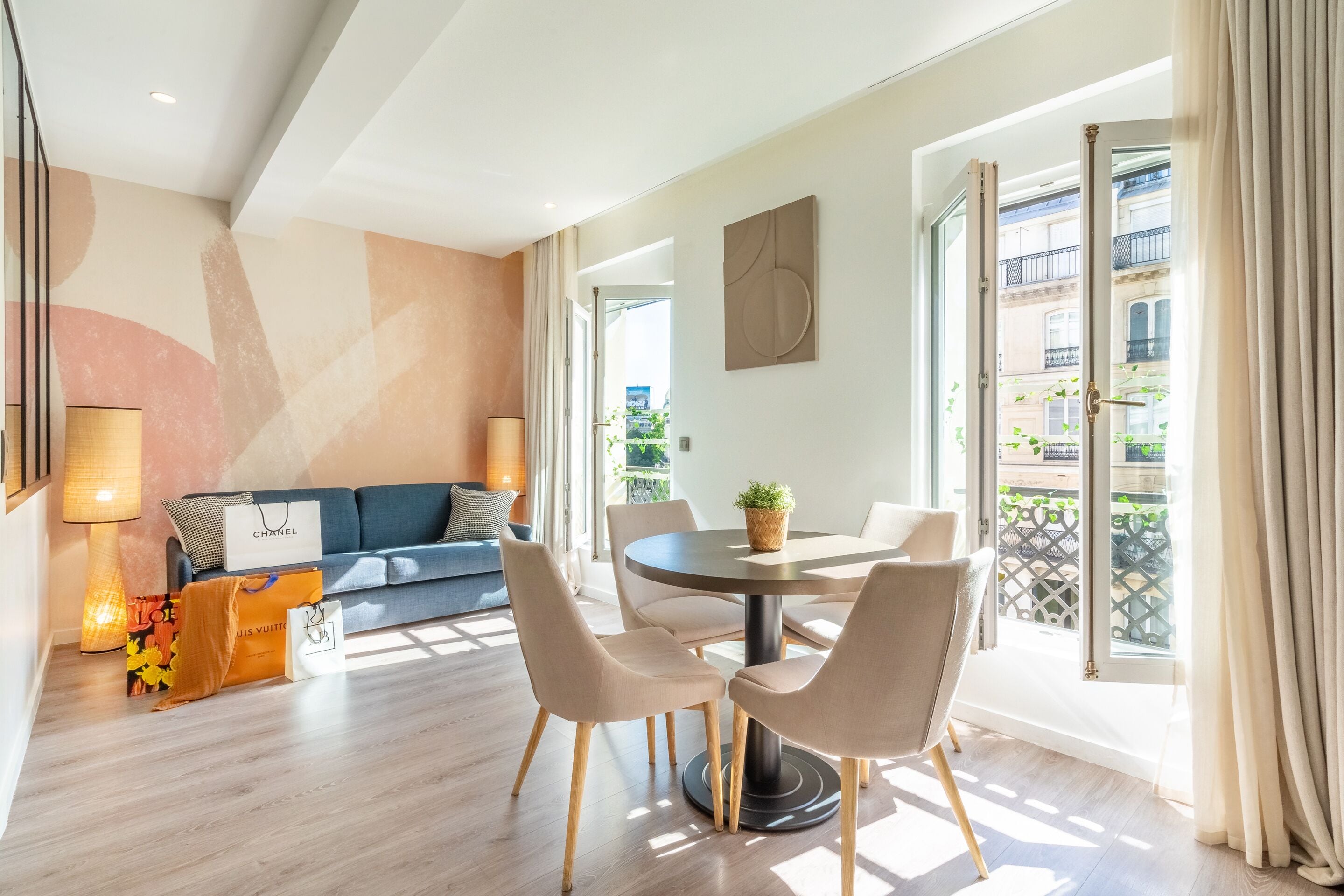 A modern living room with a sofa, a dining table with chairs, a lamp, and a view of the outside.