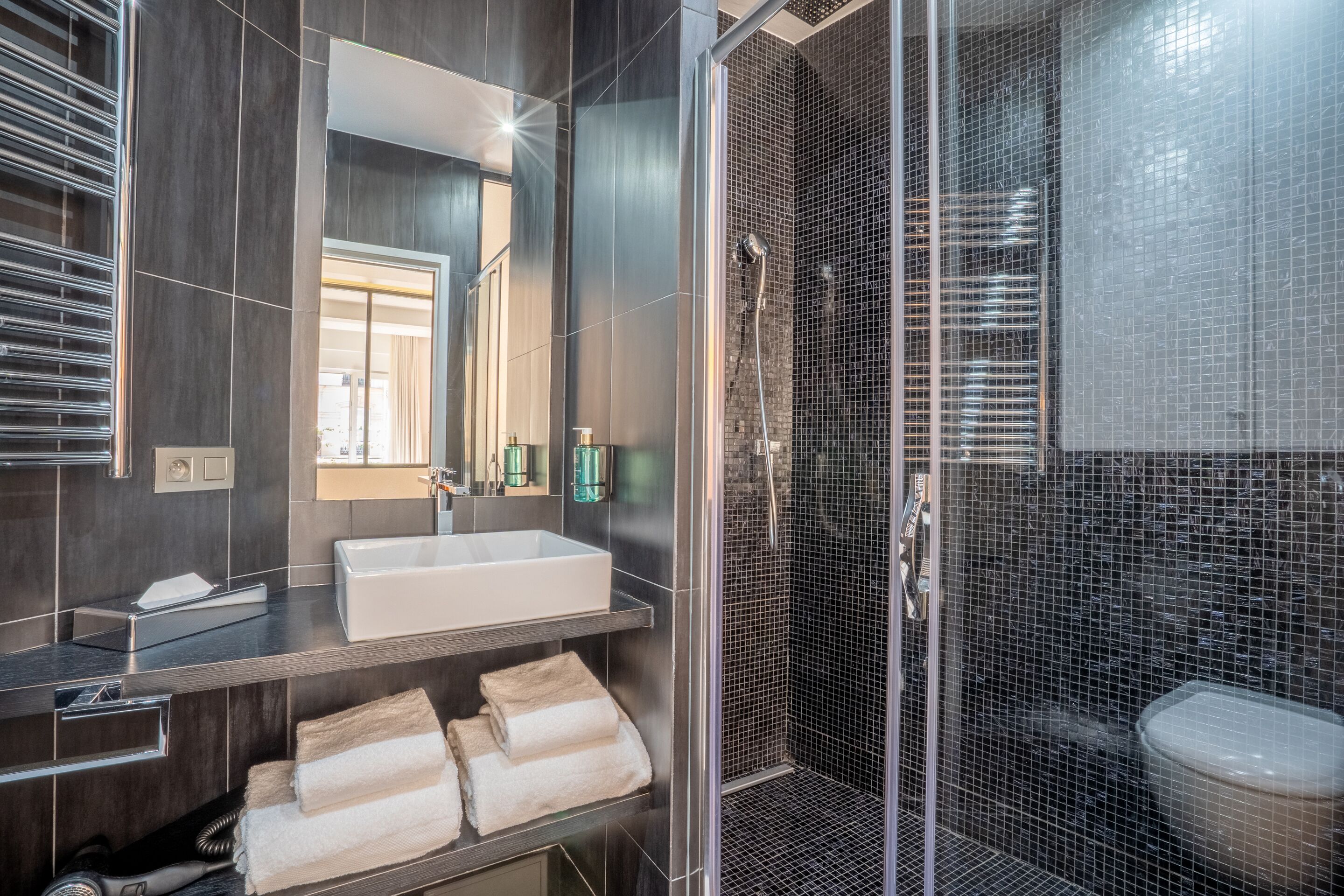 A modern bathroom with a large mirror, a white sink, and a shower enclosure.