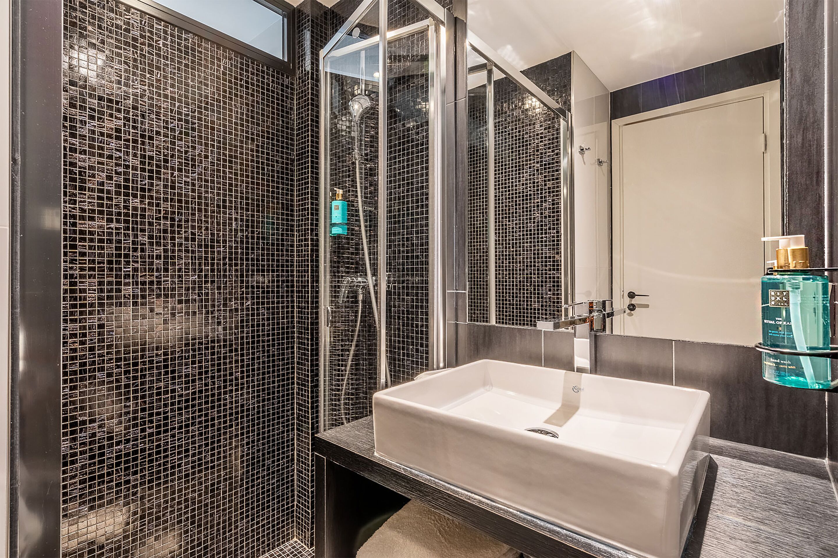 A modern bathroom with a glass-enclosed shower, a white sink, and a mirror.