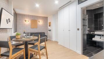 Un comedor moderno con una mesa redonda, sillas y un sofá. Cuenta con una zona de cocina con salpicadero de azulejos negros y armarios blancos.