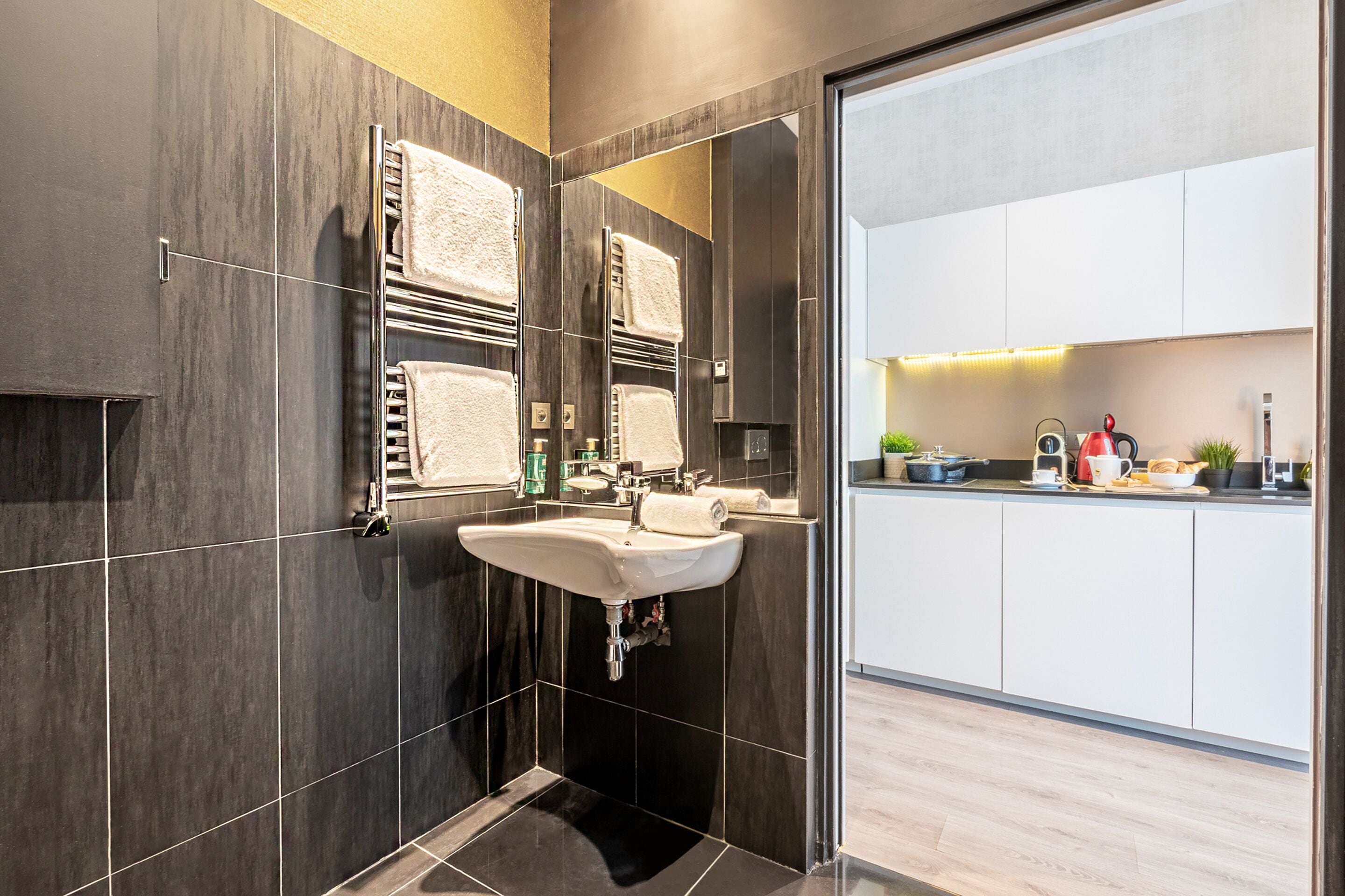 A modern bathroom with dark tiles, a white sink, and a mirror.