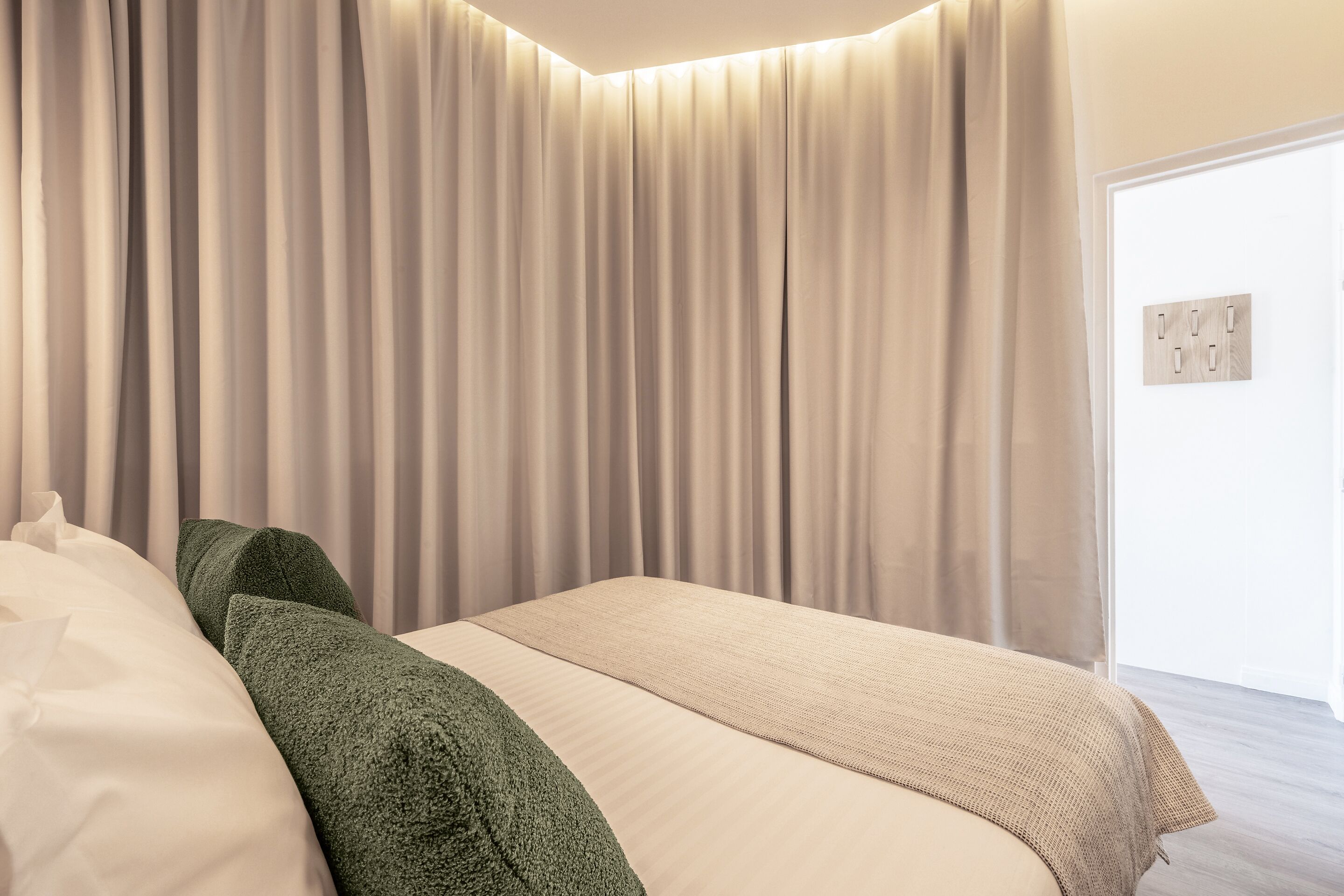 A bedroom with a bed, beige bedding, and a green pillow.