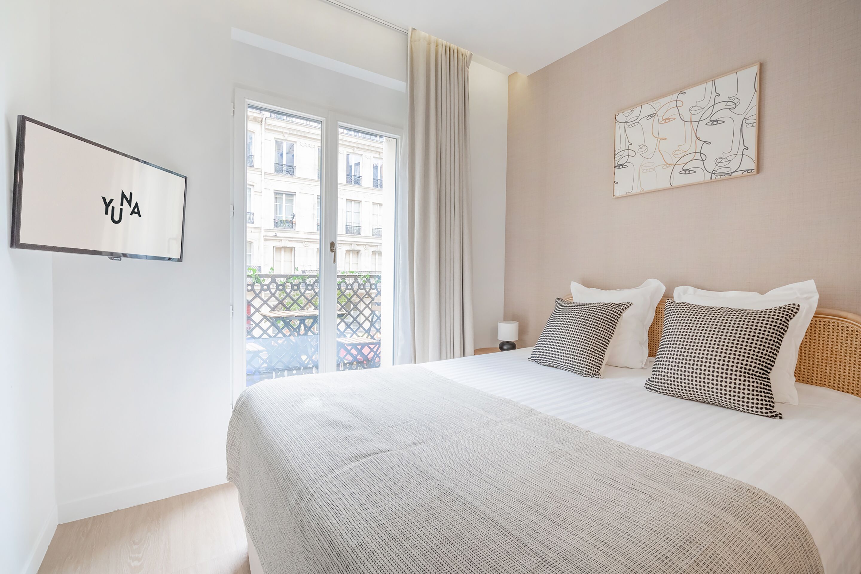 Une chambre d’hôtel avec un grand lit, une vue sur la ville par la fenêtre et une œuvre d’art encadrée au mur.