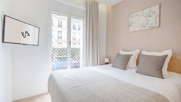 Une chambre d’hôtel avec un grand lit, une vue sur la ville par la fenêtre et une œuvre d’art encadrée au mur.