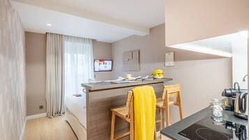 A modern kitchen with a central island, wooden chairs, a yellow towel, a kettle, and a TV on the wall.