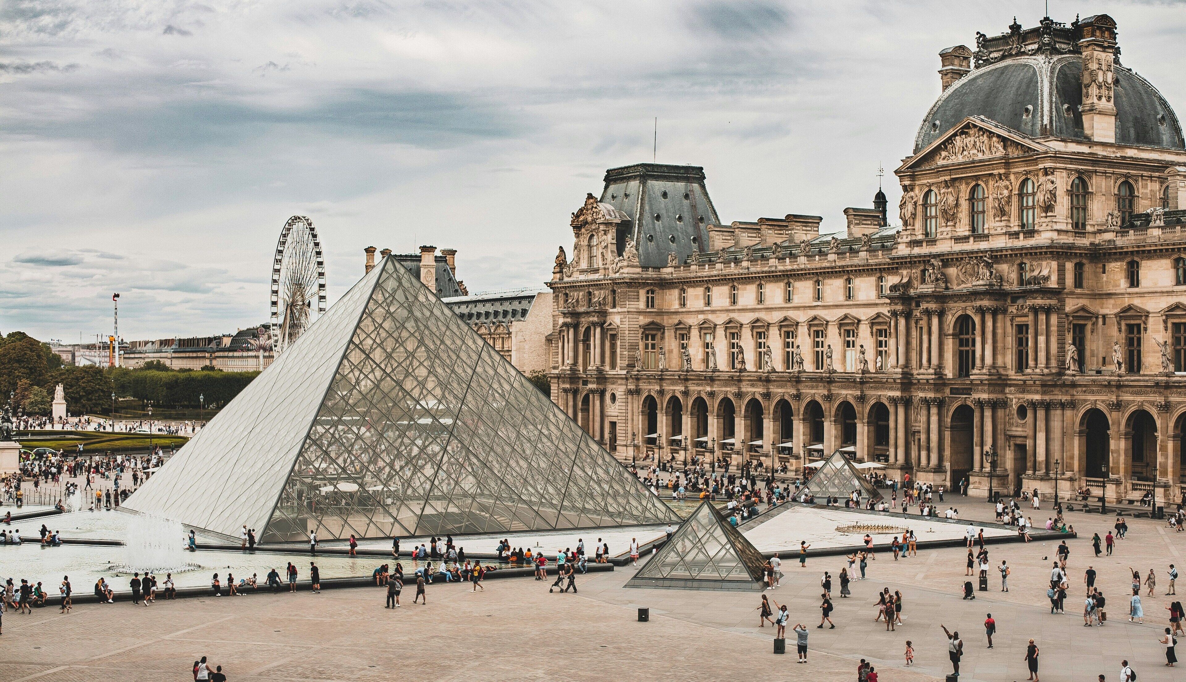 Een groot open plein met het Louvre Museum en de Piramide van het Louvre op de achtergrond.