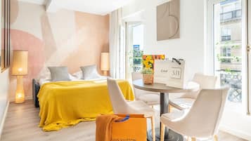A hotel room with a bed, a round table, two chairs, a lamp, and a view of the city.