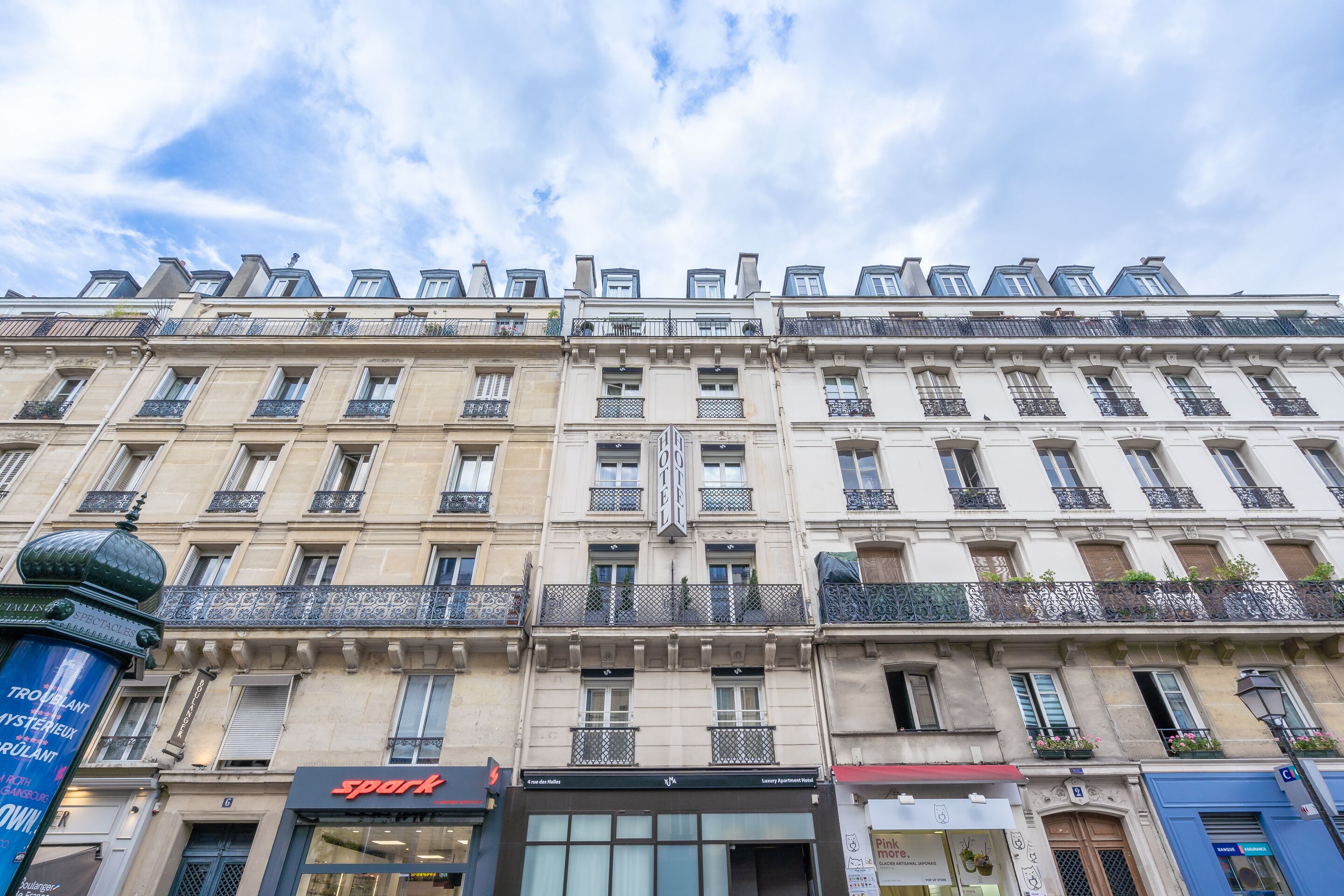 A multi-story building with a classic European architectural style, featuring balconies with wrought iron railings and a central entrance with a sign.