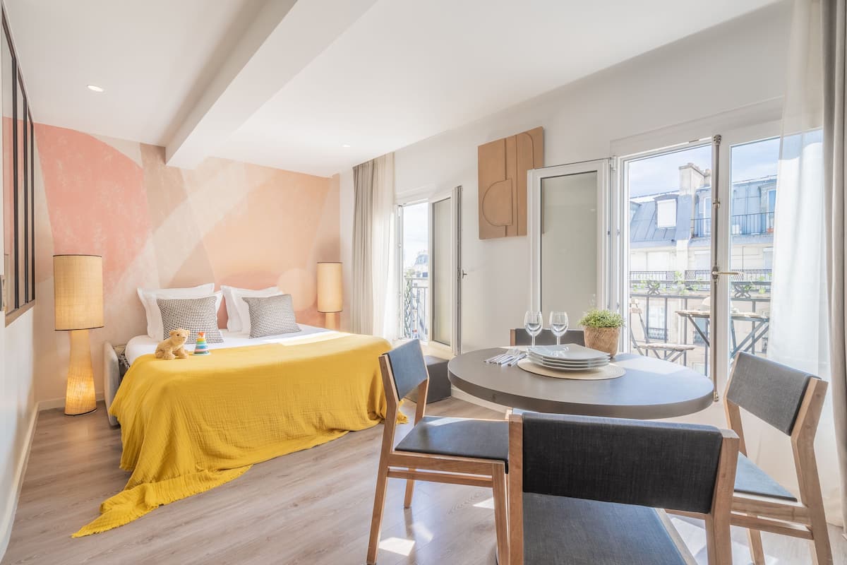 Moderni hotellihuone, jossa on sänky, ruokapöytä ja parveke, jolta on näkymä.
