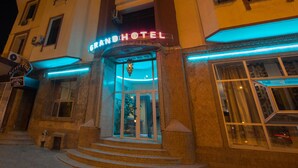 El exterior del Grand Hotel, con un llamativo letrero de neón, una entrada tradicional y una escalera que conduce a ella.