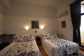Una habitación con dos camas, una mesita de noche, un calentador en la pared y una ventana con cortinas.