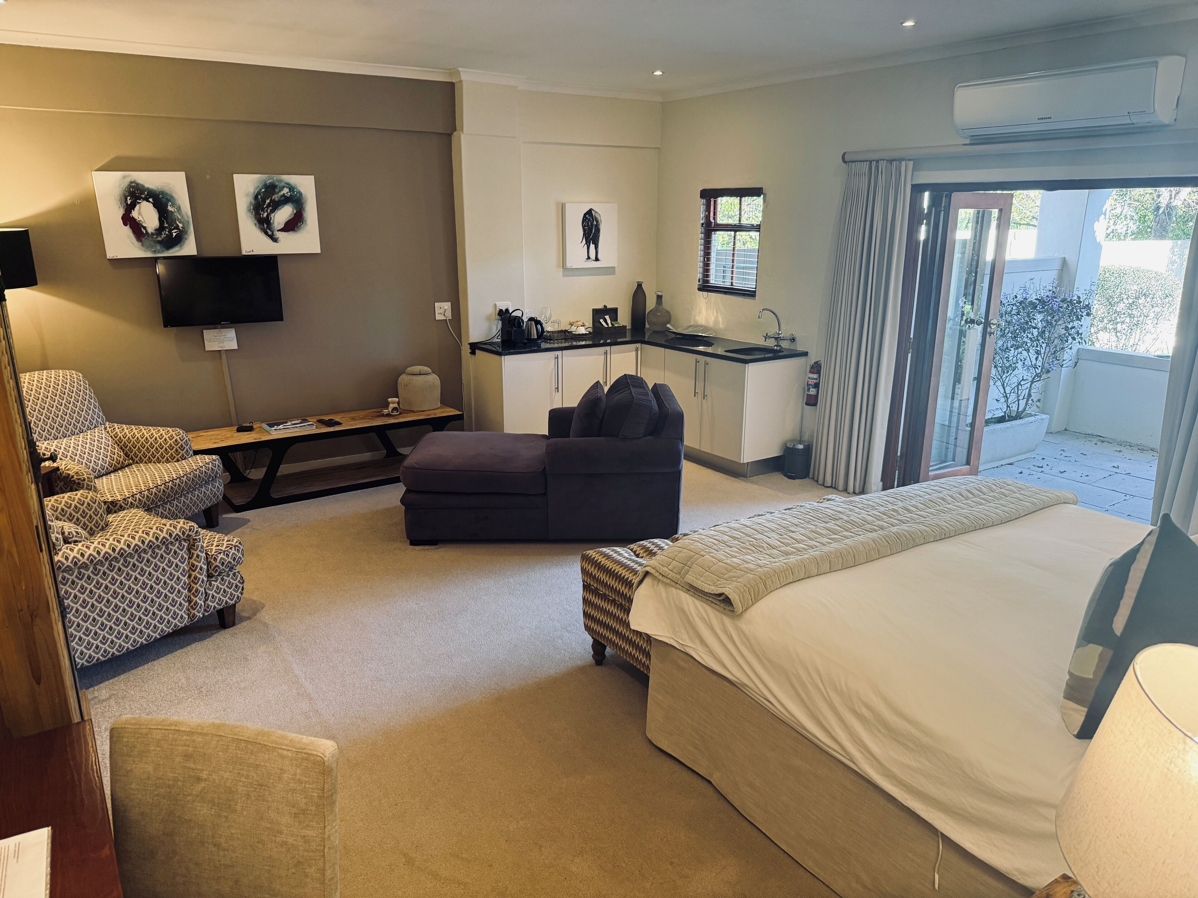 A hotel room with a bed, a sofa, a desk, a TV, and a small kitchenette.