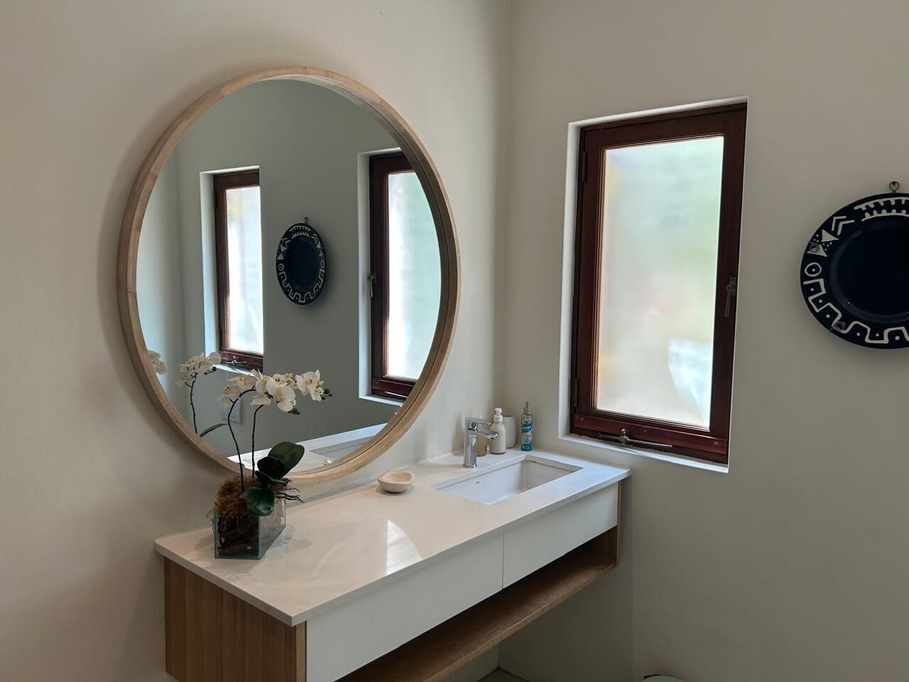 Een badkamer met een ronde spiegel, een witte wastafel en een raam met uitzicht.